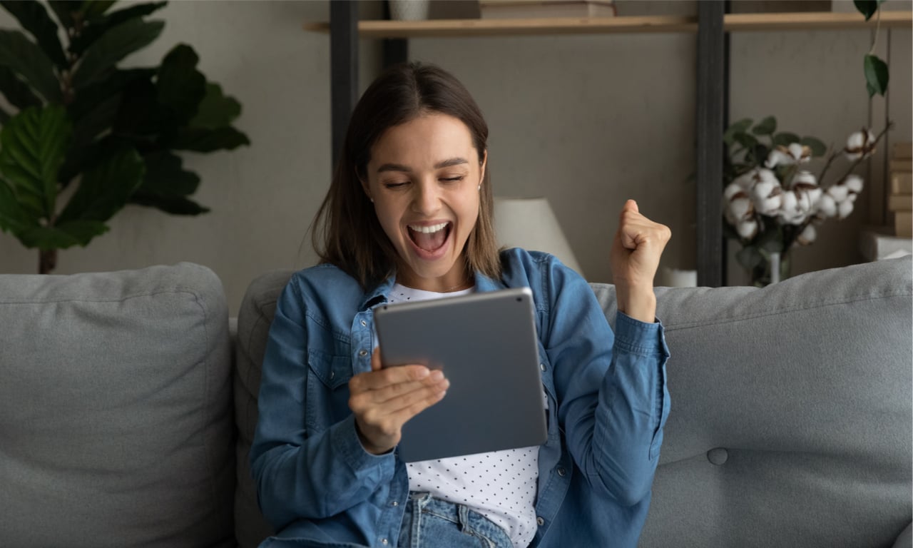 woman at home on the couch cheering at the ipad in her hand which probably has GMS as a meta partner on it